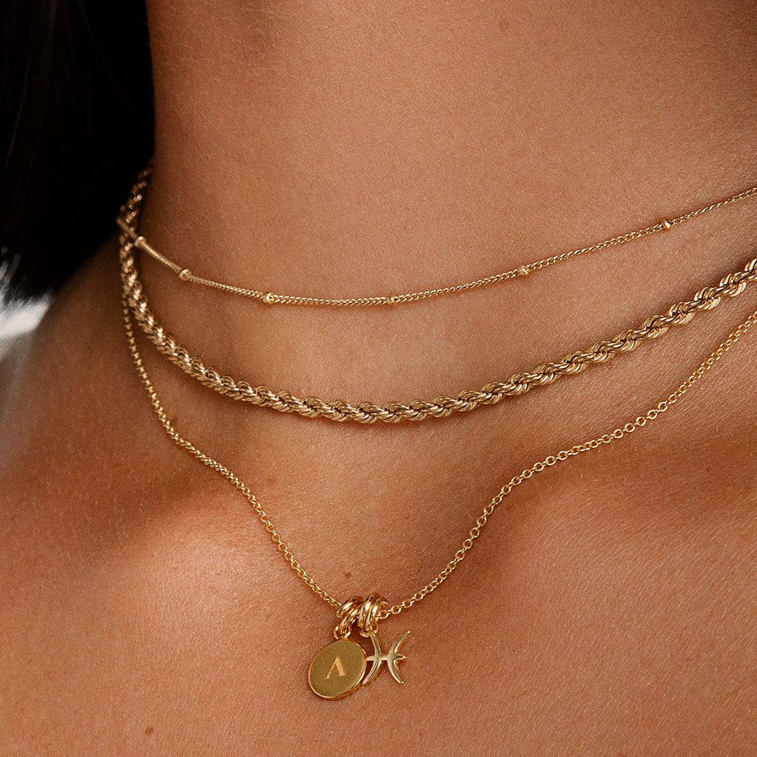 A gold rope chain necklace on the neck, layered with other chains, close up