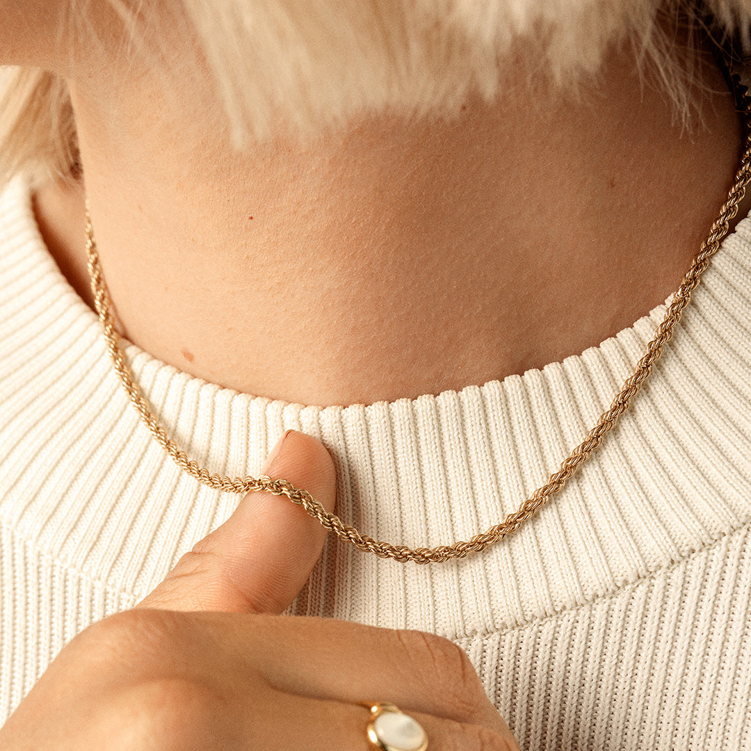 A gold rope chain necklace on neck, close up