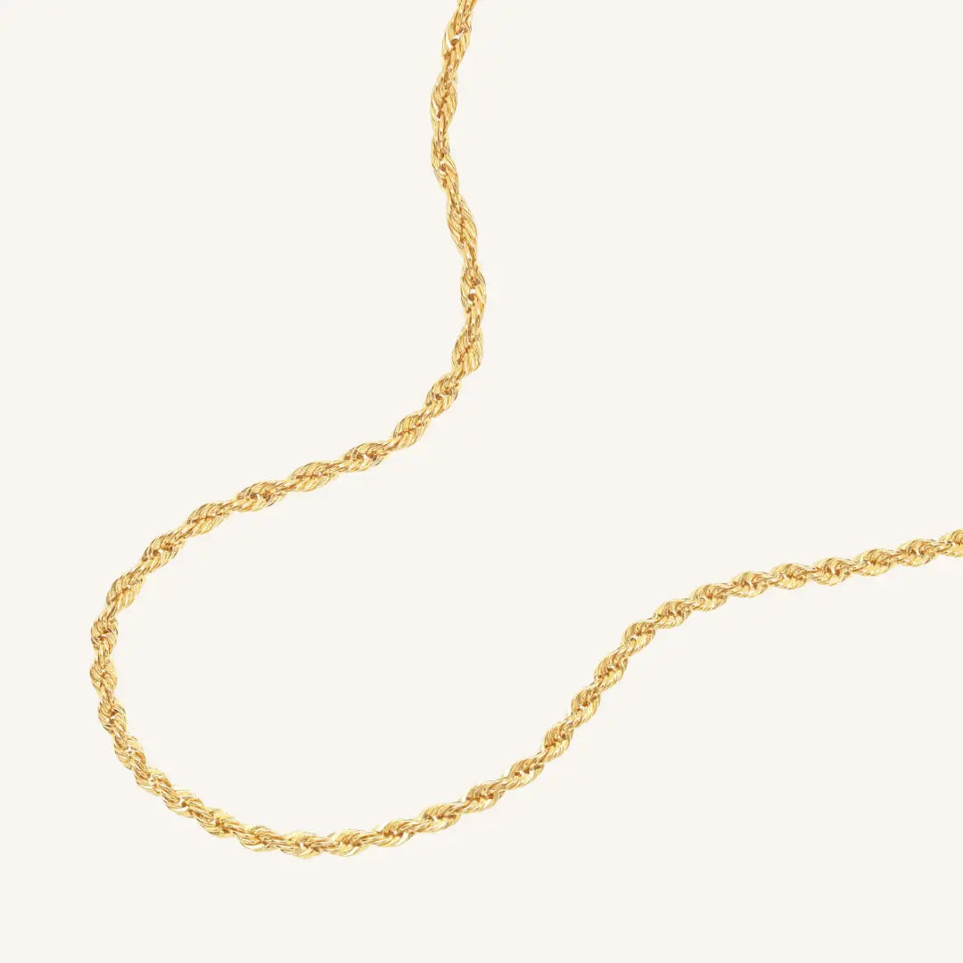 A gold rope chain necklace on a plain background.