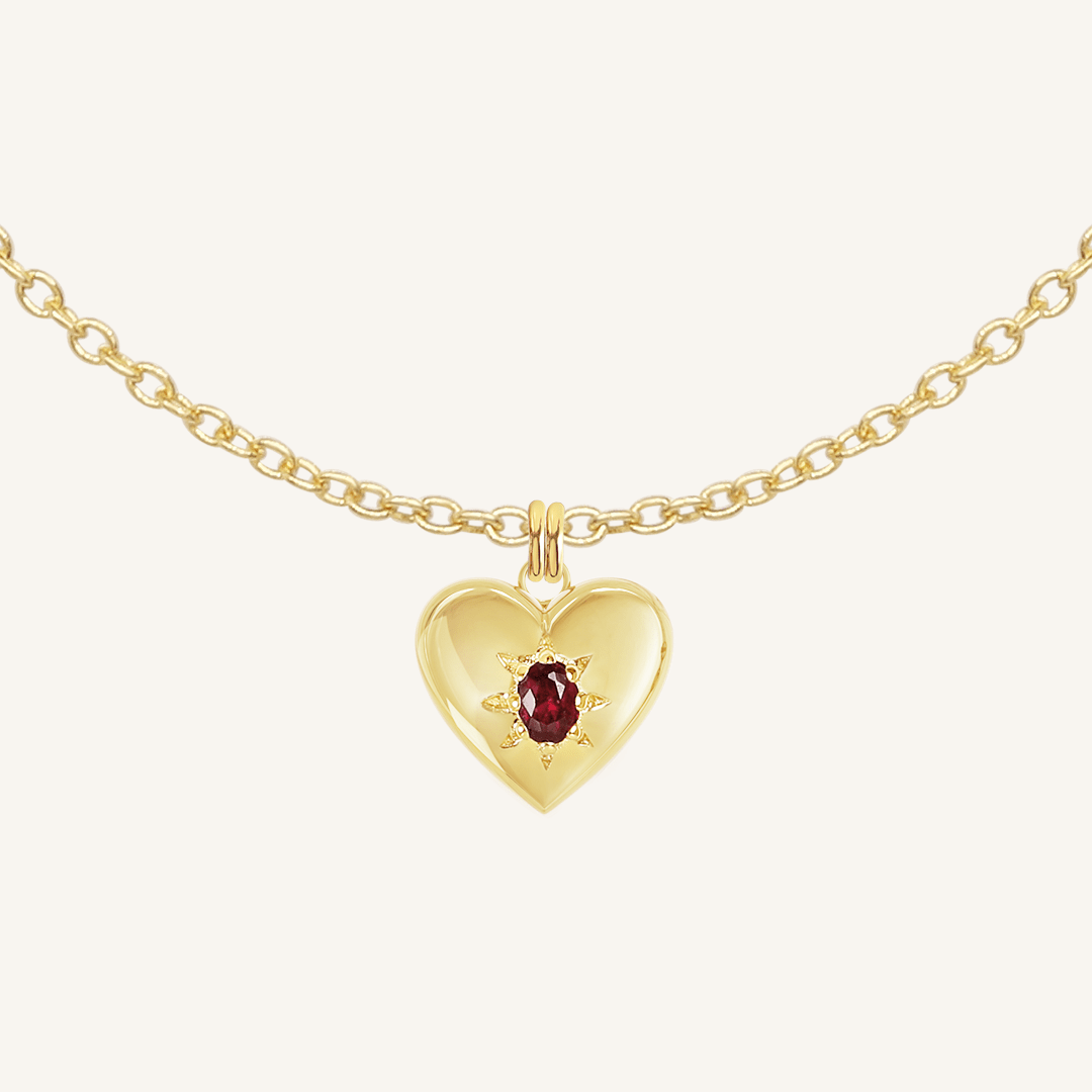 gold heart shaped charm with deep red oval cubic zirconia on plain chain on white background