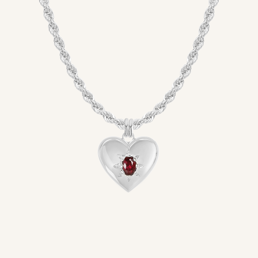 silver heart shaped charm with deep red oval cubic zirconia on rope chain on white background