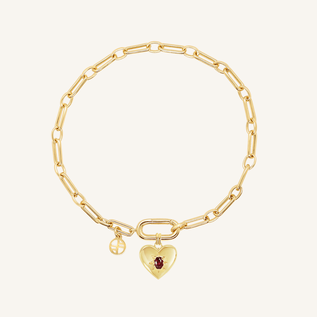 gold heart shaped charm with deep red oval cubic zirconia attached to create link bracelet on white background