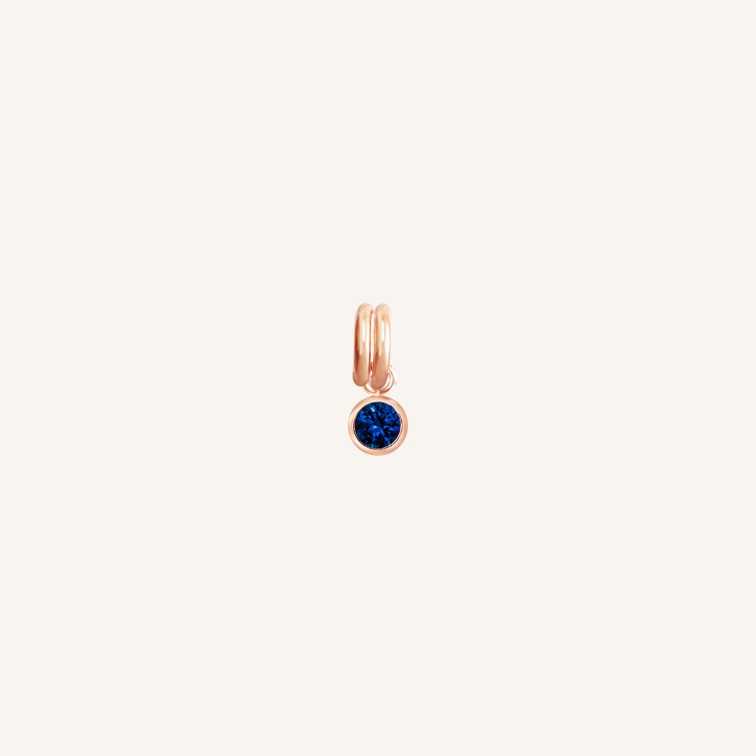A round September birthstone charm with a blue cubic zirconia, set in rose gold.