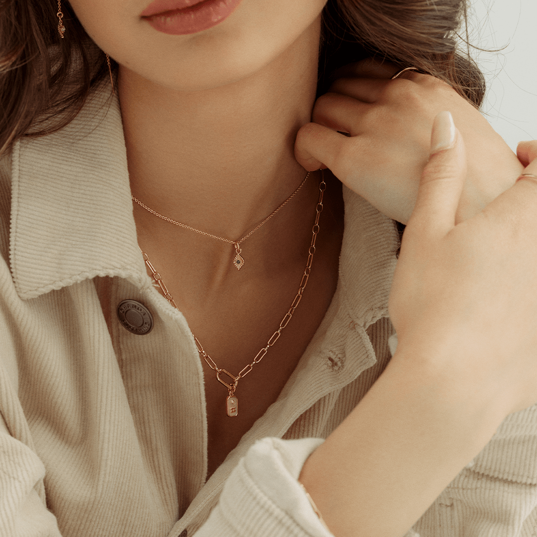 A silver-colored birthstone charm with a central blue cubic zirconia, representing September, on chain on neck
