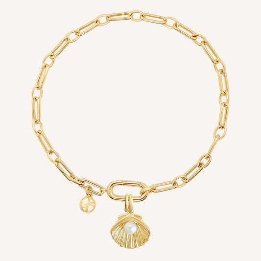 A gold-colored chain bracelet with a shell shaped charm with a pearl in the middle