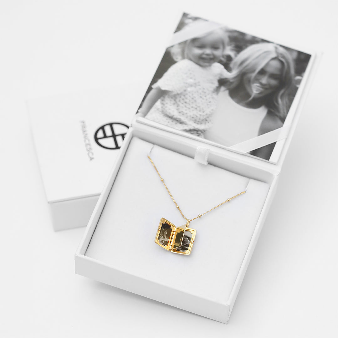 A gold locket with a laser engraved inscription of 'You'll always be my baby' on a chain and presented in a box with a photo