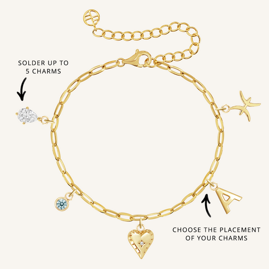 A gold-tone bracelet with paperclip links and multiple charms, including a heart, a star, and a letter, with an extender chain.