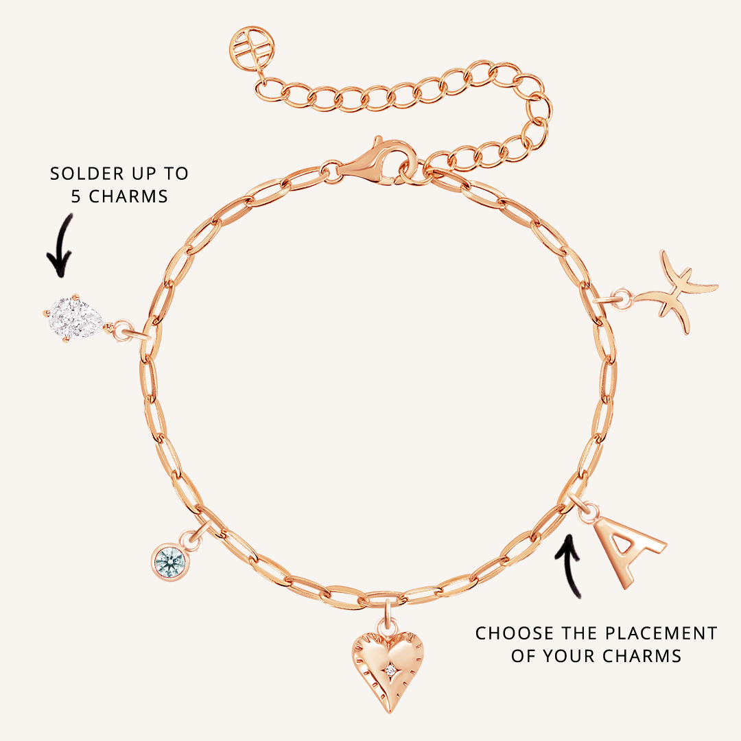 A gold-tone bracelet with paperclip links and multiple charms, including a heart, a star, and a letter, with an extender chain.