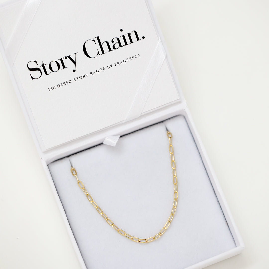 A gold chain necklace with paperclip links, displayed in a white box
