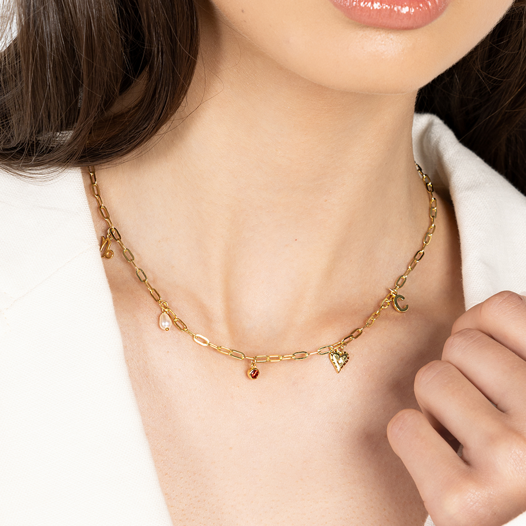 A gold chain necklace with paperclip links and multiple charms, worn around models neck