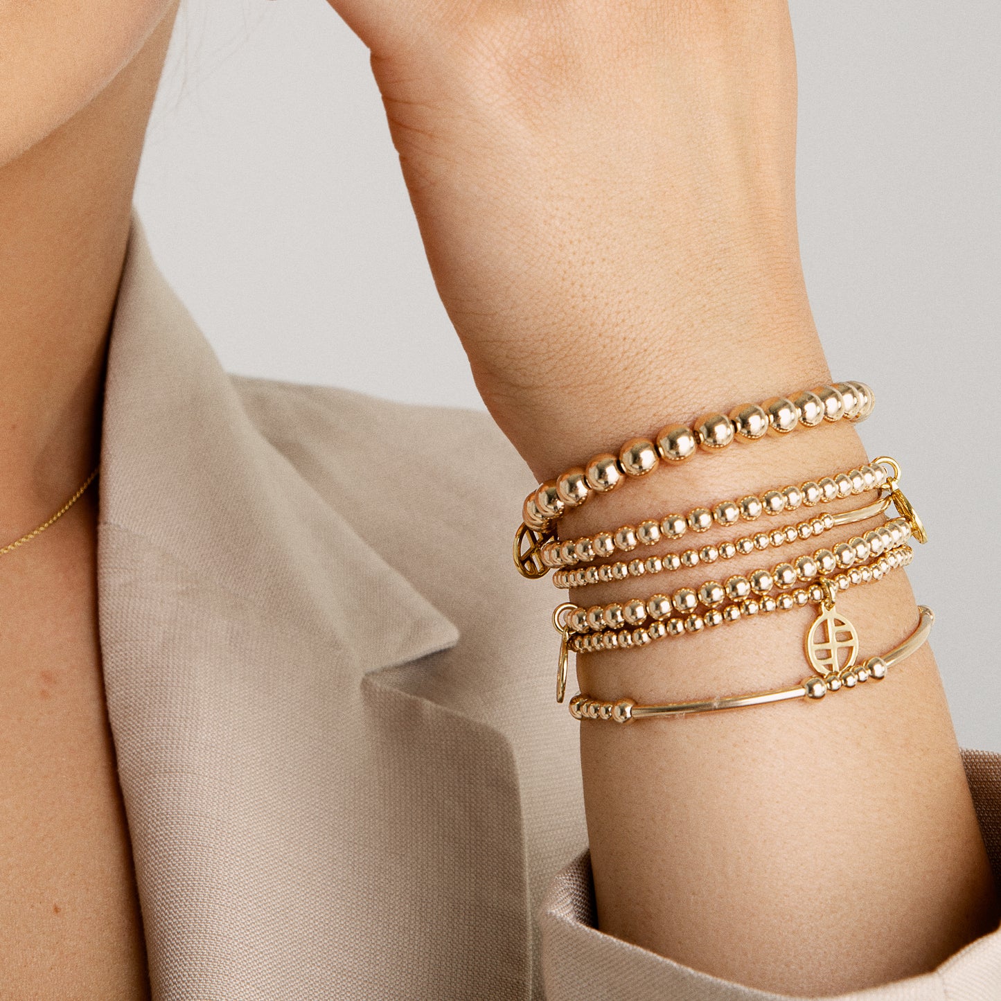 A gold-tone bracelet with spherical beads and a Francesca logo, stacked with other bracelets, worn on models wrist