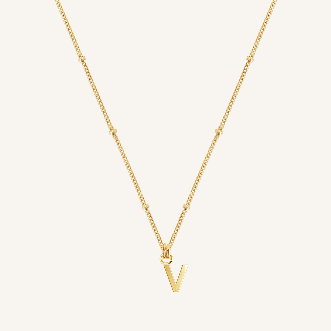 Gold necklace with a 'V' pendant on a light beige background