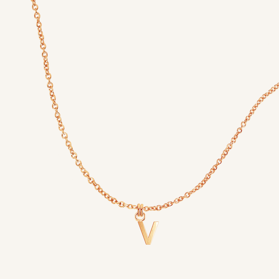 Rose gold necklace with a 'V' pendant on a light beige background