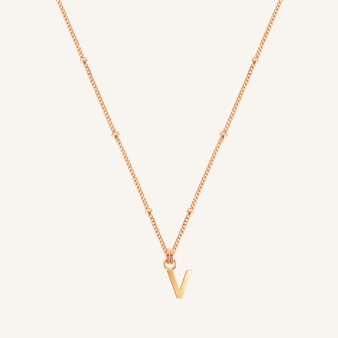 Rose gold necklace with a 'V' pendant on a light beige background