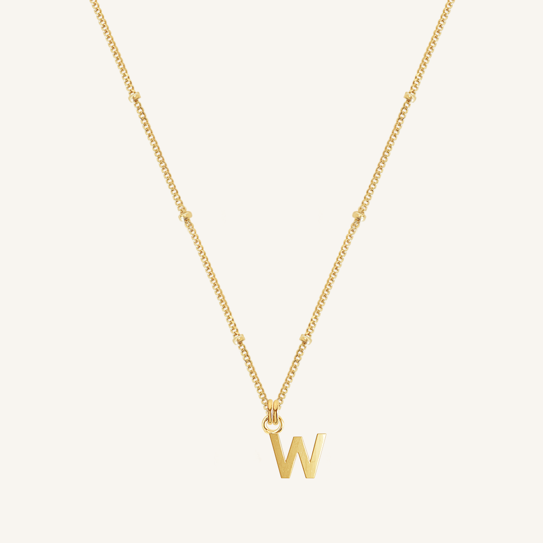 Gold necklace with a 'W' pendant on a light beige background