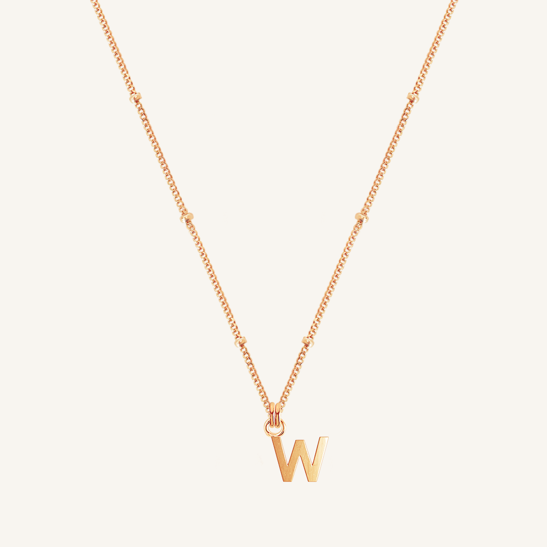 Rose gold necklace with a 'W' pendant on a light beige background