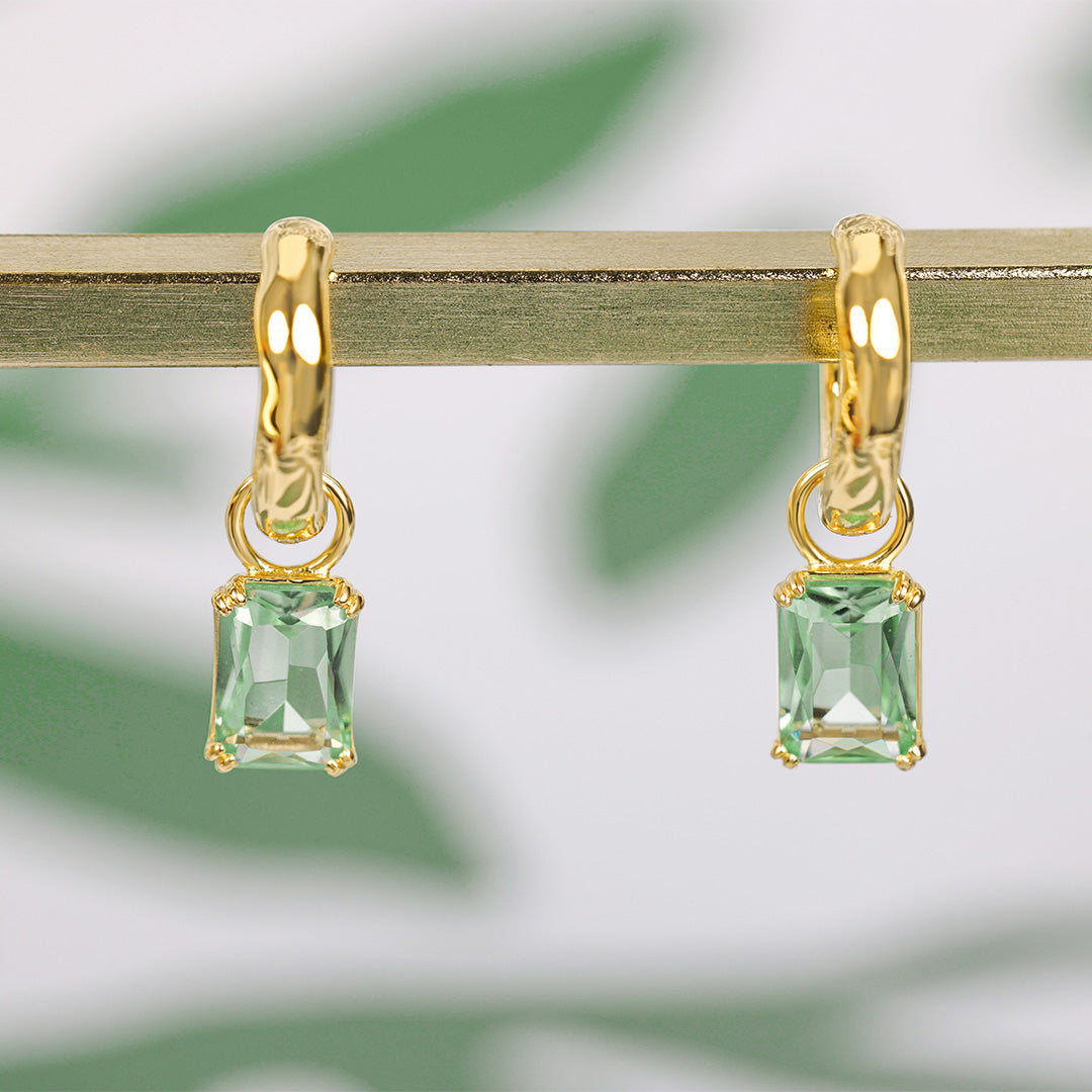 Gold earrings with green gemstones on a blurred green background