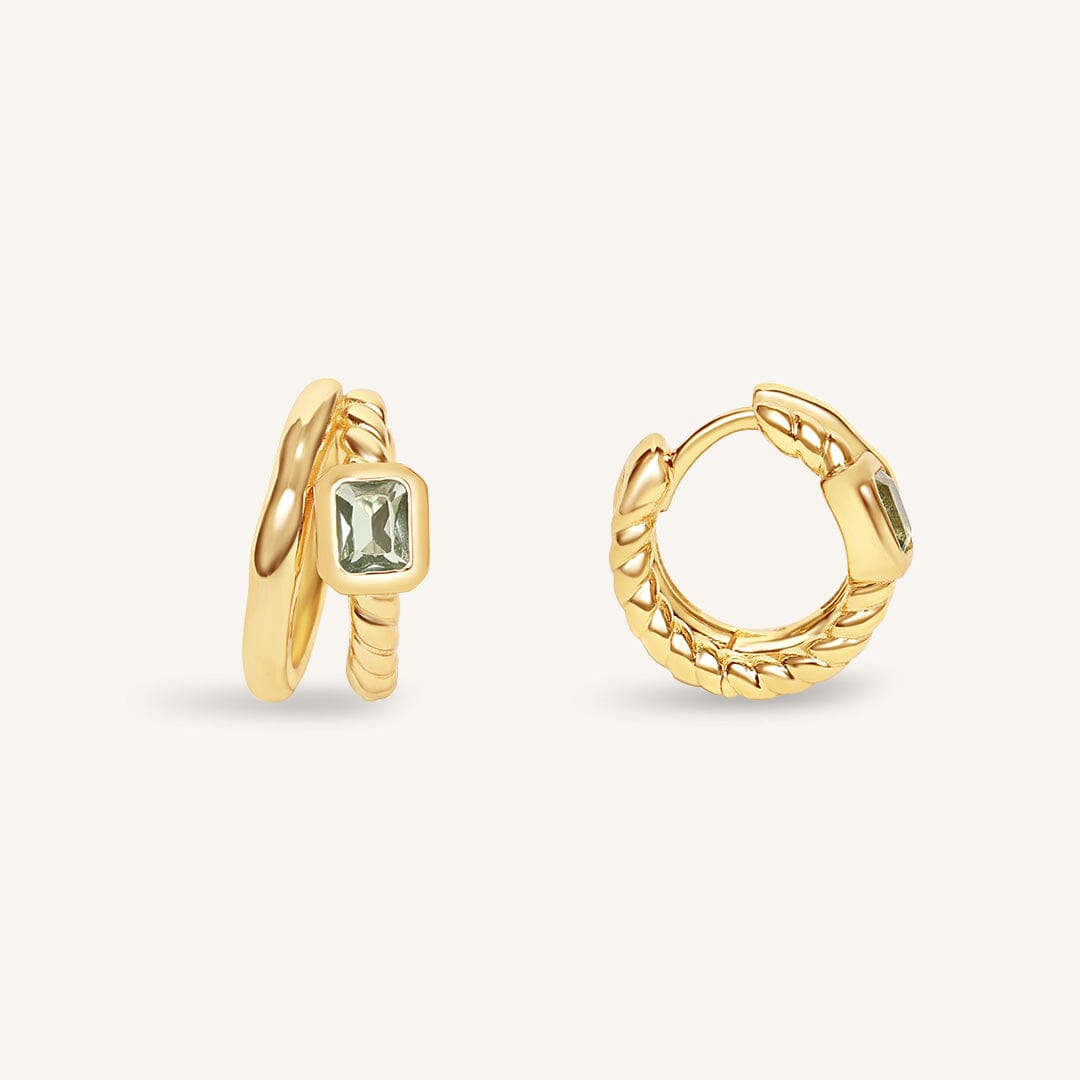Gold hoop earrings with a central gemstone on a light beige background