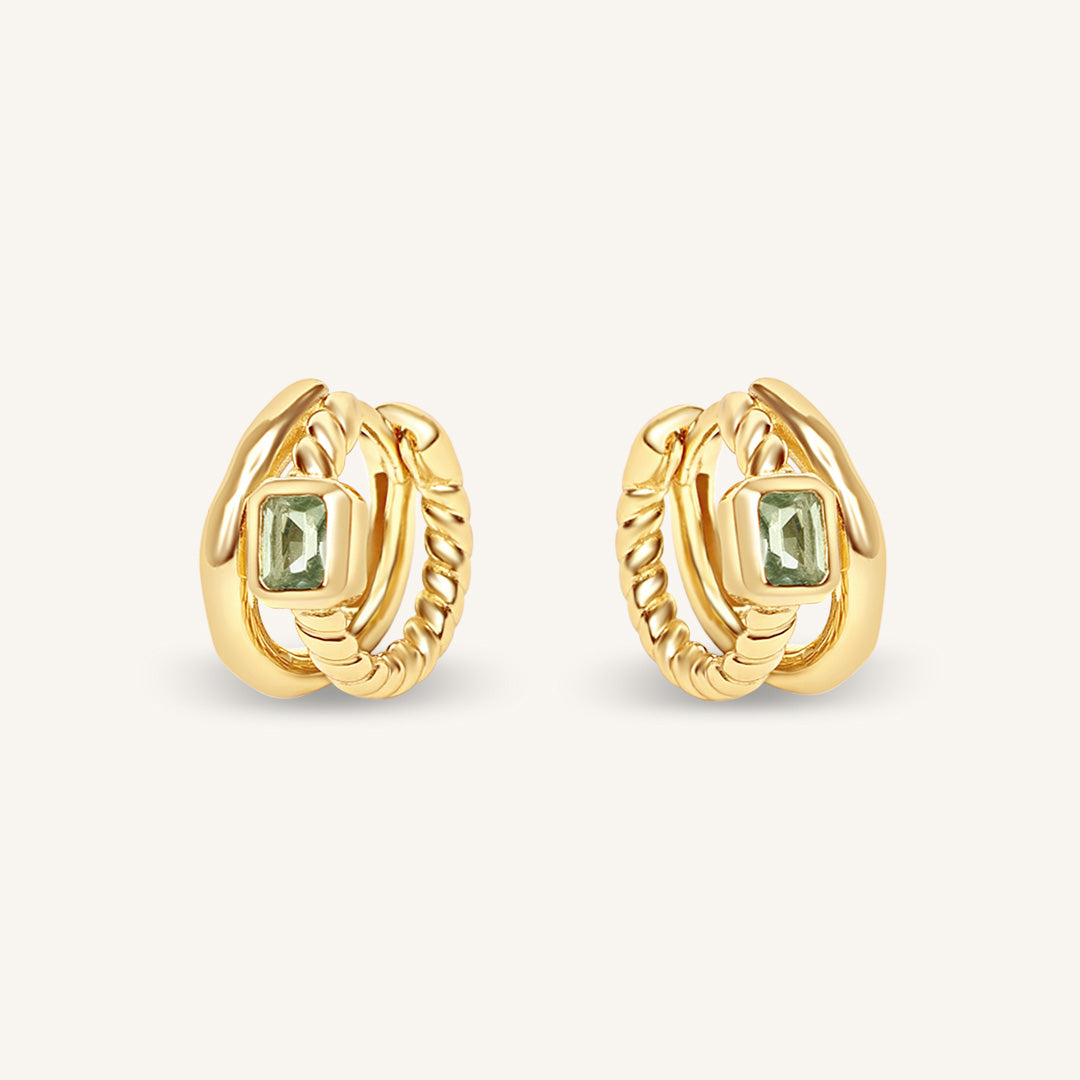 Gold hoop earrings with green gemstones on a light beige background
