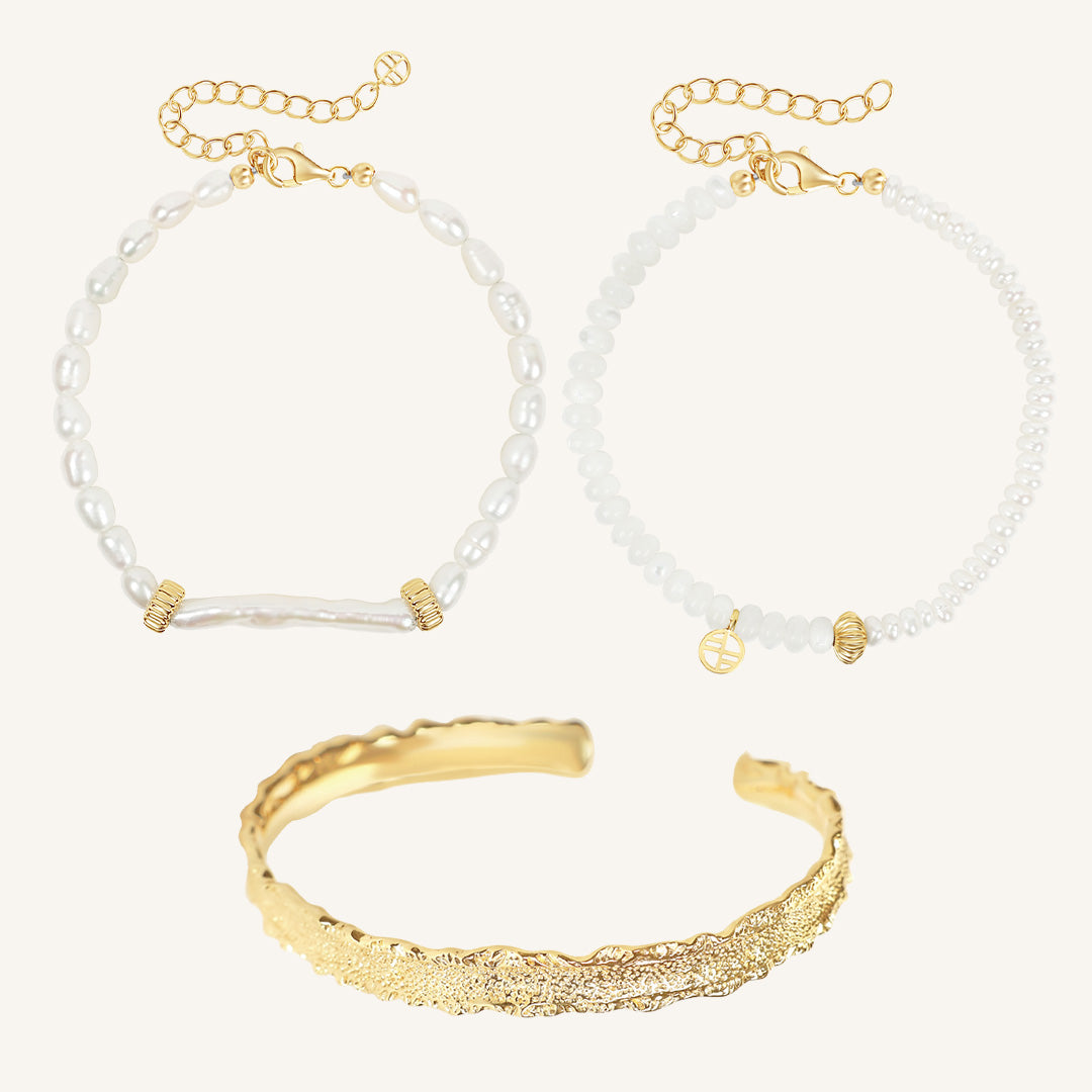Gold bracelet and two pearl beaded bracelets on a light gray background