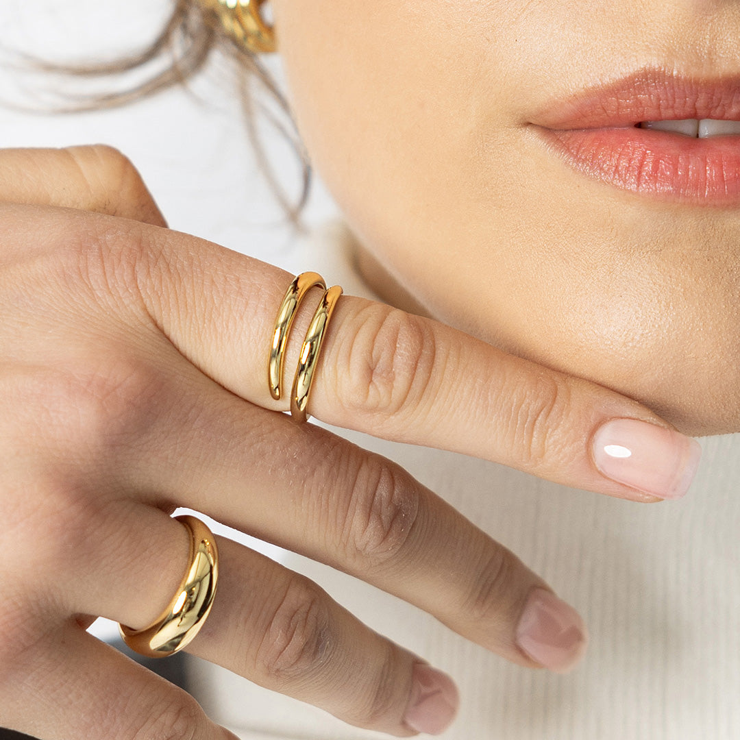 Close-up of a person's hand wearing two gold rings on a neutral background