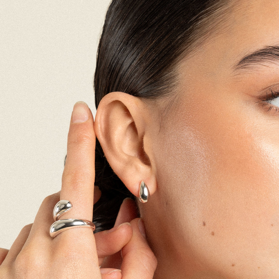 A pair of silver stud earrings with a smooth finish, worn in models ear
