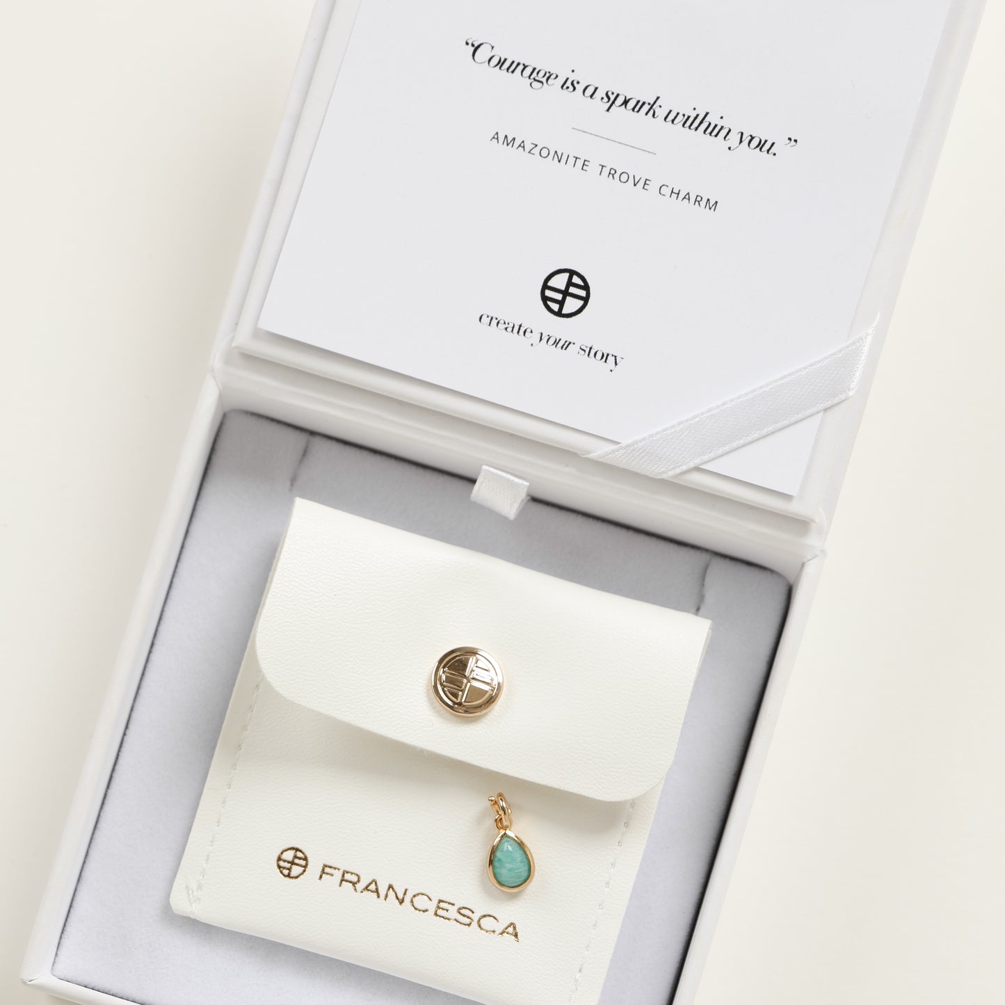 A gold charm with a teardrop-shaped amazonite stone set in a bezel in white box