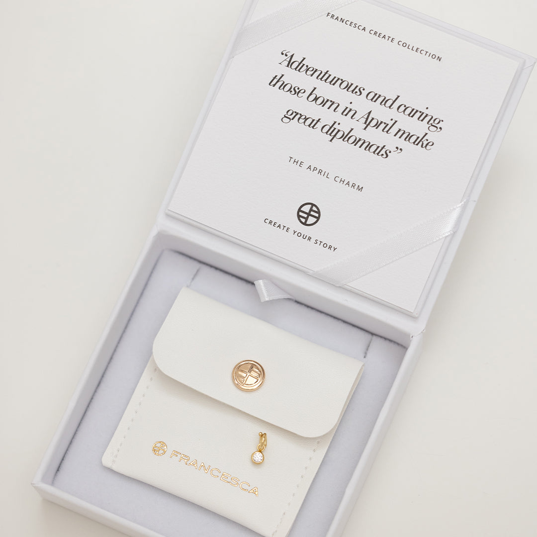 Round gold charm with bezel-set white cubic zirconia representing the April birthstone in white box.