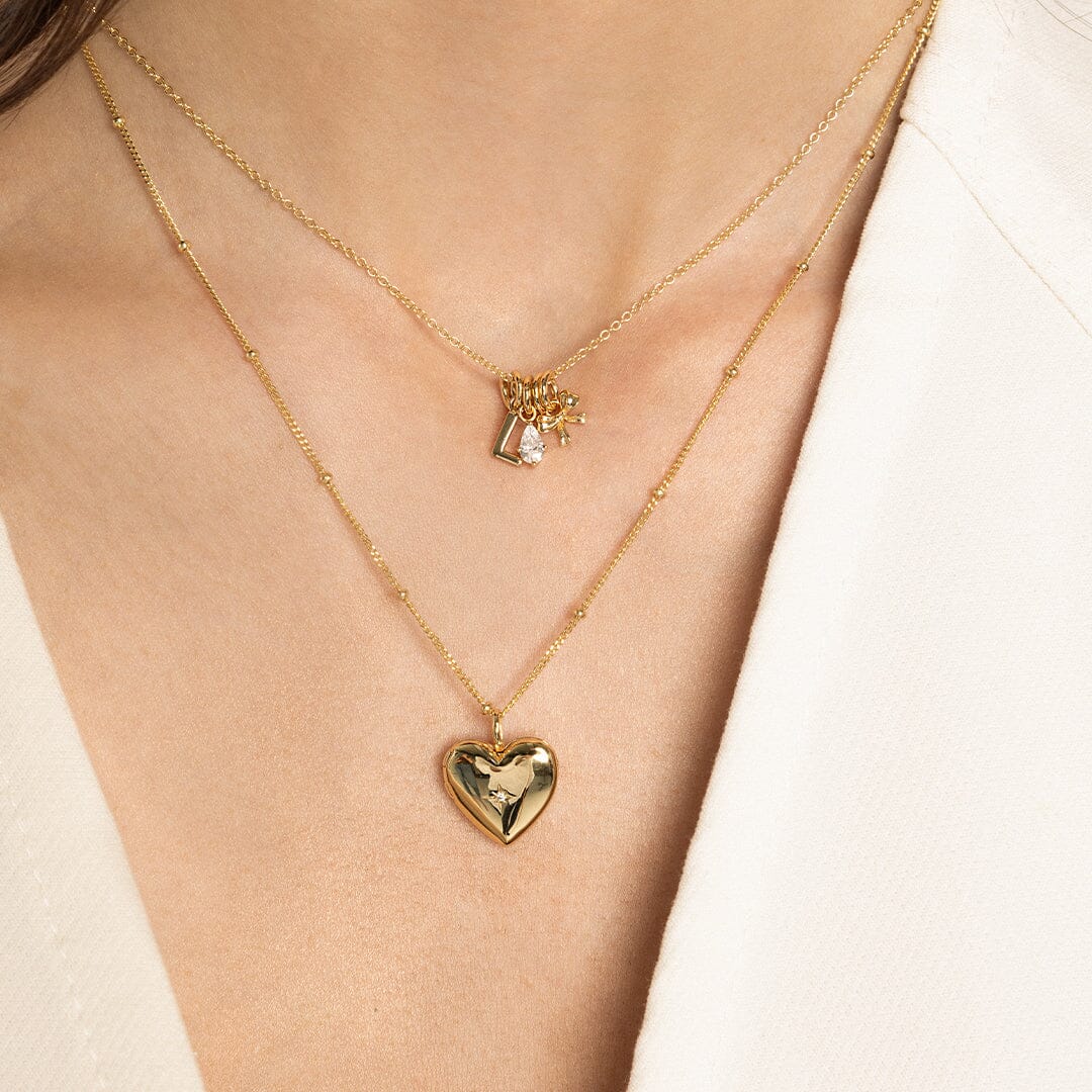 A teardrop-shaped cubic zirconia charm with a gold metal tone, on gold chain with other charms, close up on models neck