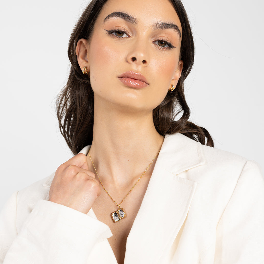 A gold bevel photo locket opened to display photographs inside on a chain, around the neck on lady