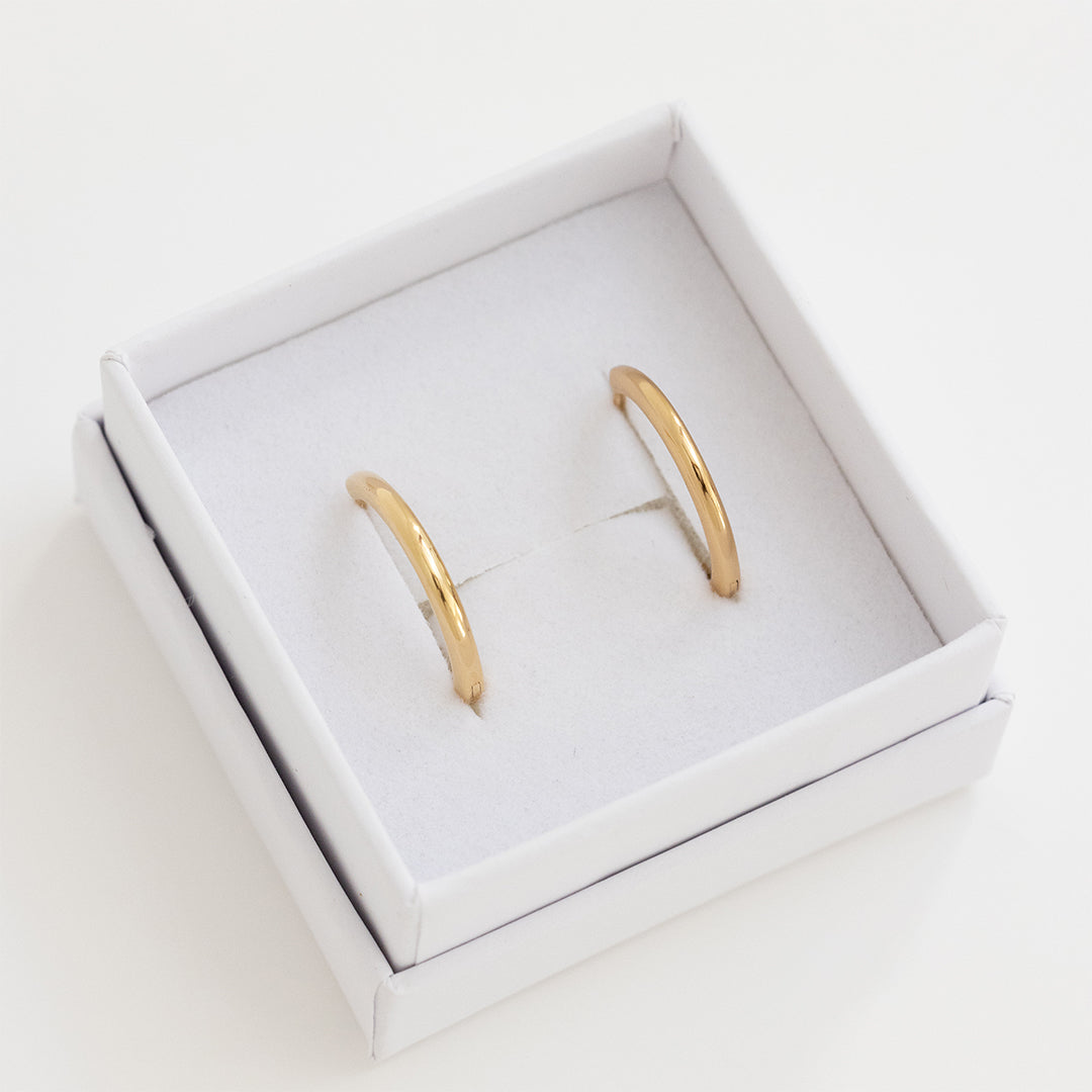 A pair of gold-tone hoop earrings, displayed in a white box