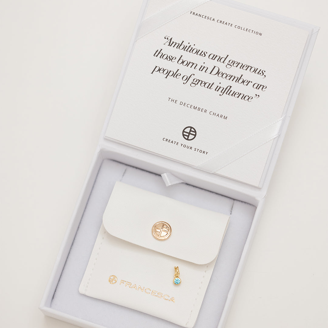 Round gold charm with bezel-set turquoise cubic zirconia representing the December birthstone in white box.