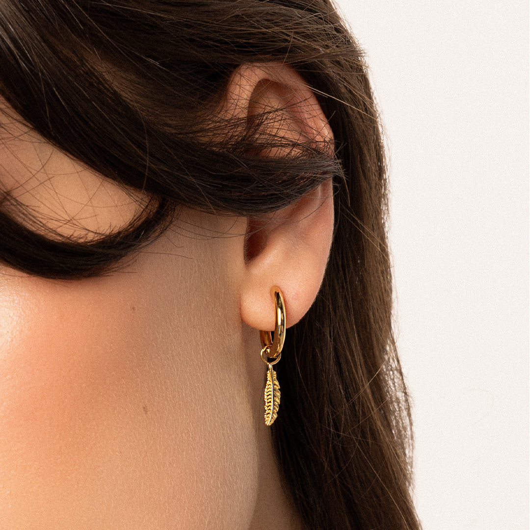 A set of two gold hoop charms with a feather design, on gold hoops, in ear
