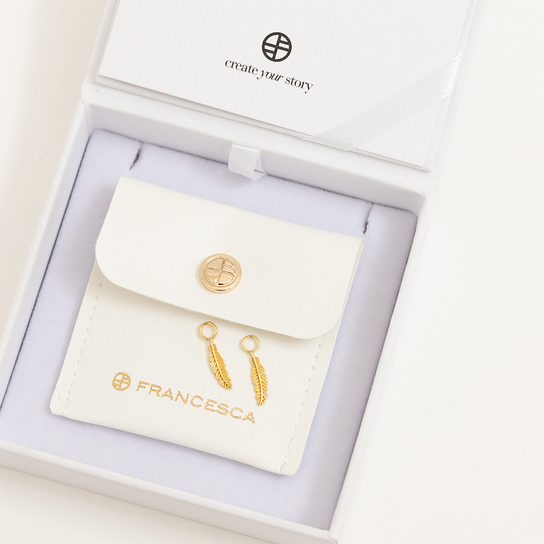 A set of two gold hoop charms with a feather design, in white box.
