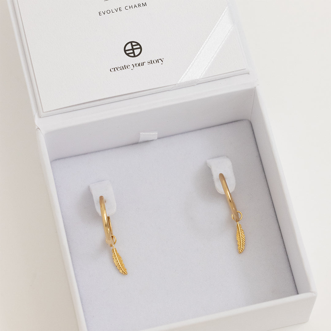 A set of two gold hoop charms with a feather design, on gold hoops