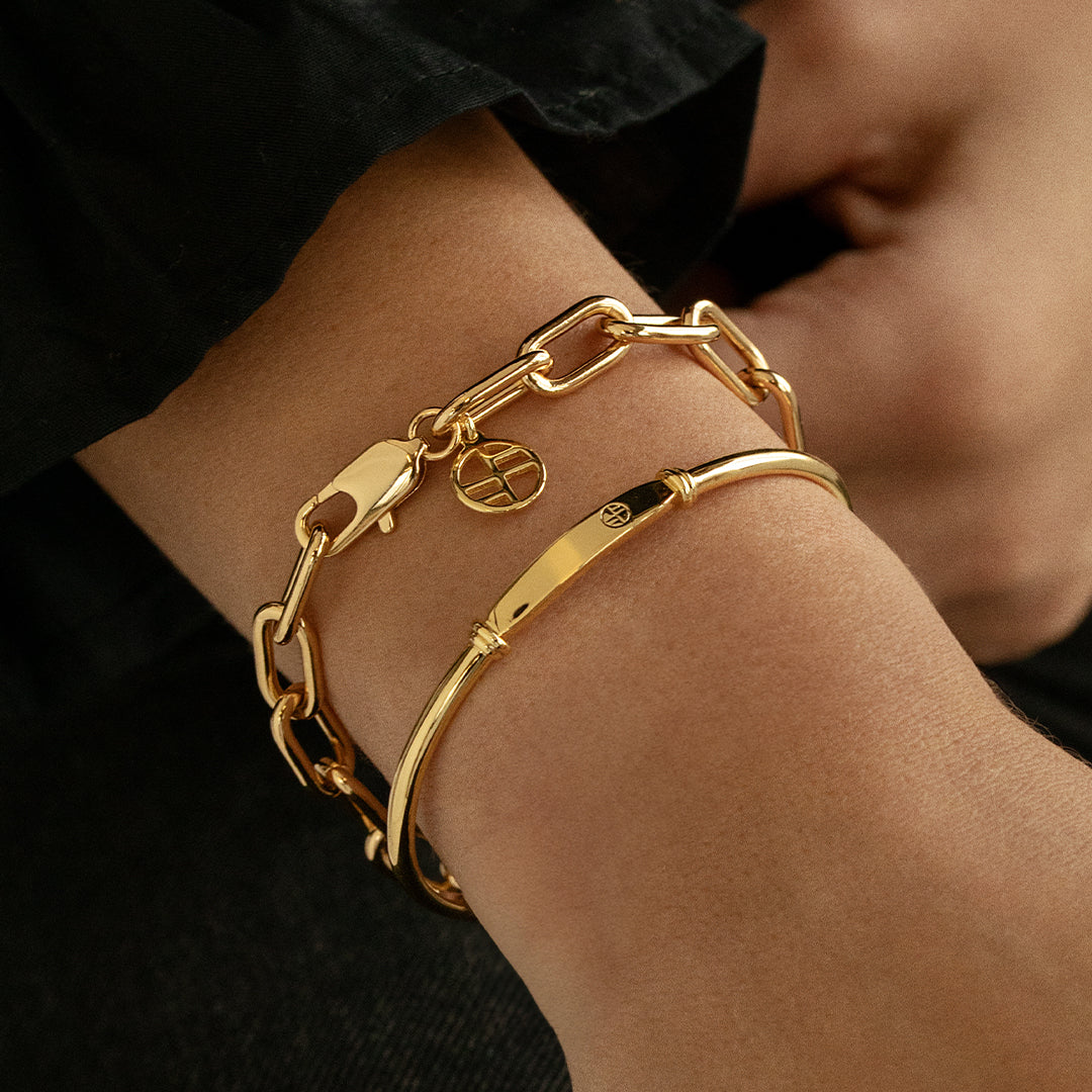 close up of A chunky link style bracelet in gold tone, featuring a clasp closure, worn on wrist