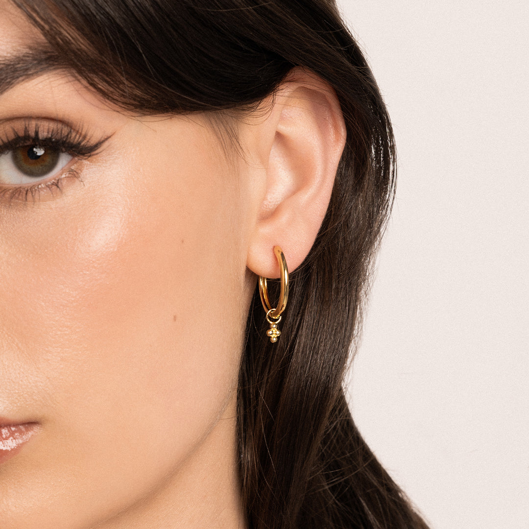 A pair of gold-tone hoop earrings with bobble details, worn in models ear