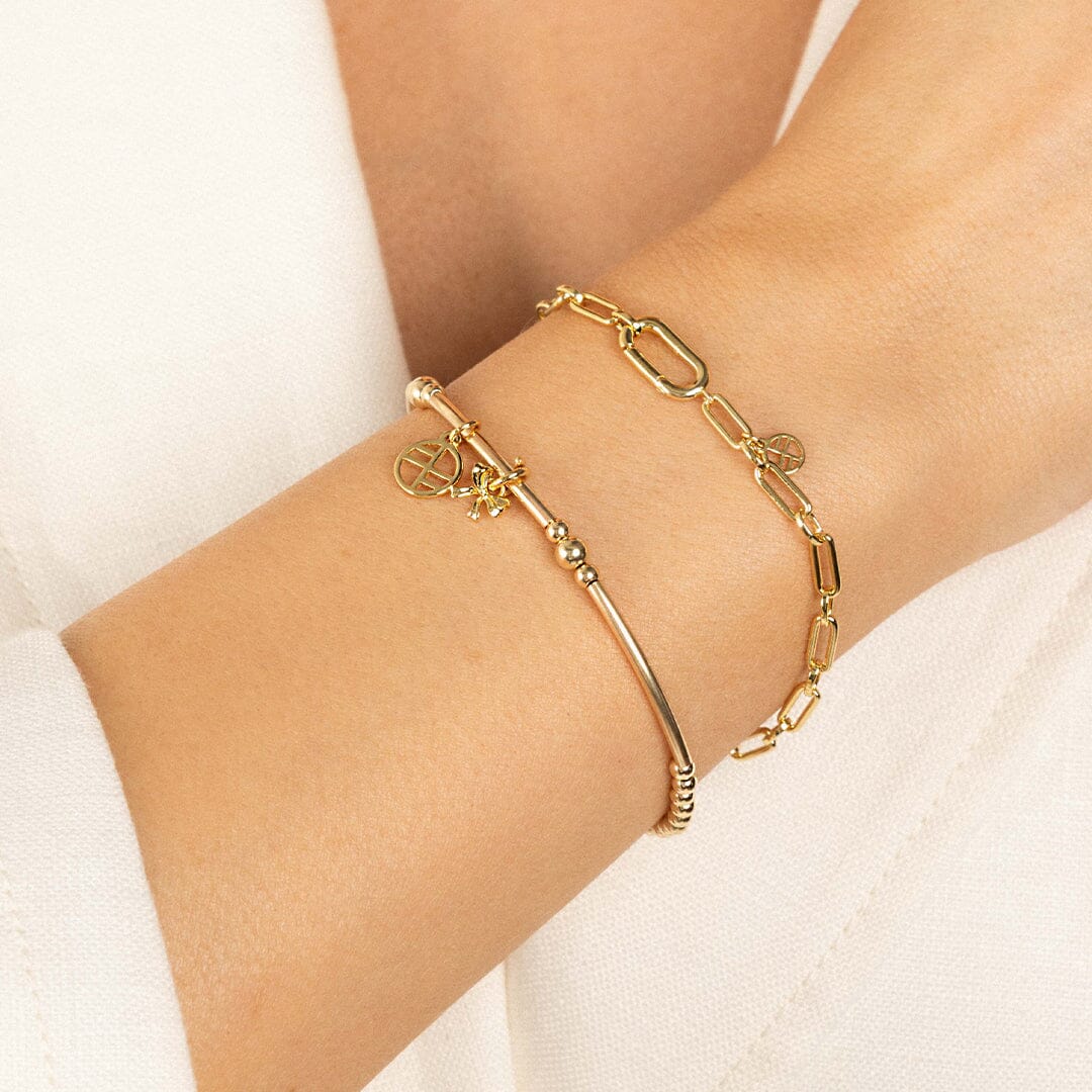 A small gold bow charm attached to bracelet, worn on models wrist