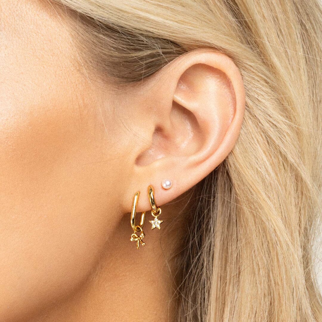 A set of two gold hoop charms with a bow design on hoops, in ears