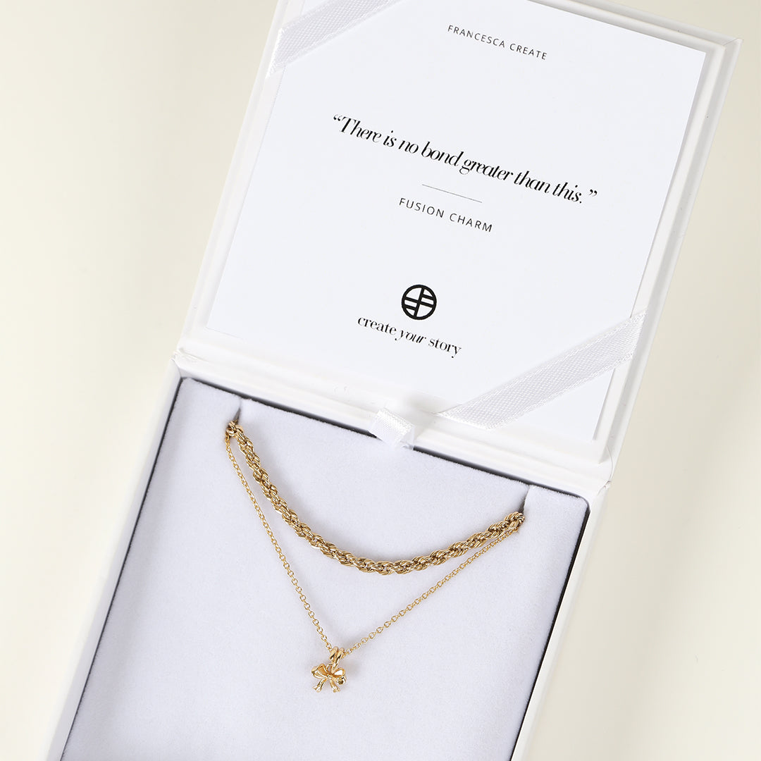 A coloured necklace featuring a bow-shaped charm on a plain chain, displayed in white box