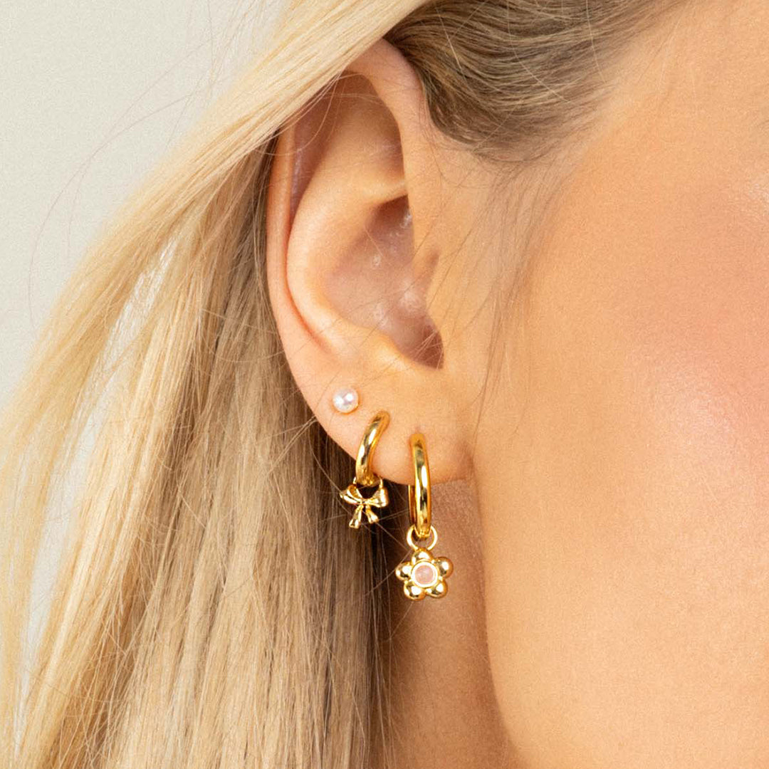A set of two gold hoop charms with a bow design, on hoops, in ears
