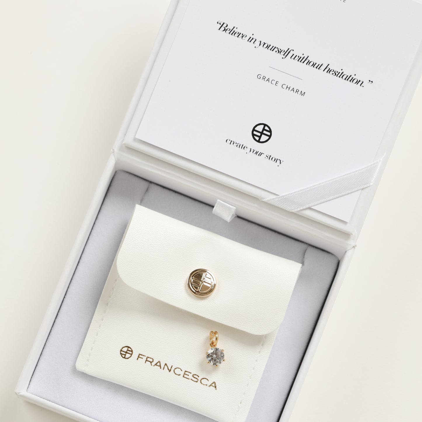A round gold cubic zirconia charm, displayed in white box