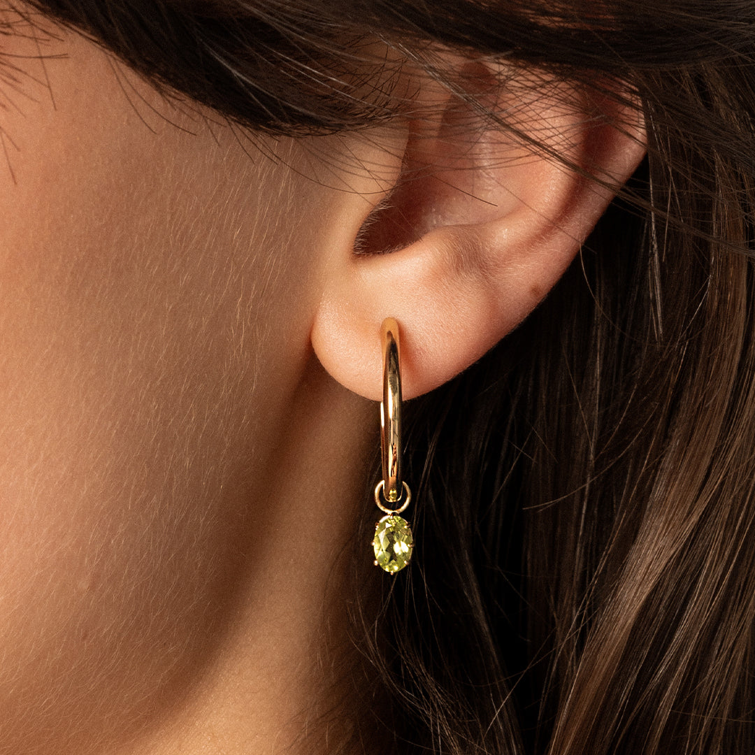 A set of two gold hoop charms with olive green stones, attached to hoops, close up in the ear