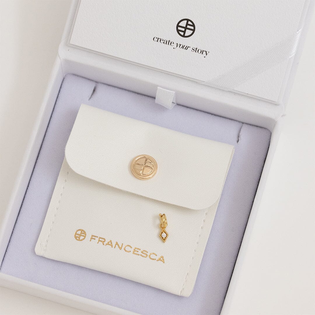 A small, diamond-shaped gold charm with a white stone in the center, in a white box.