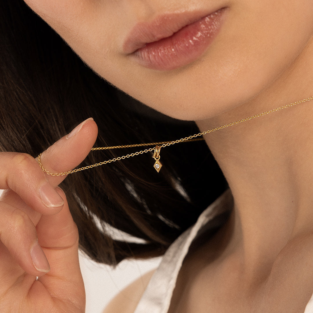 A small, diamond-shaped gold charm with a white stone in the center, on gold chain, around neck
