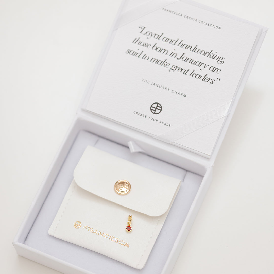 Round gold charm with bezel-set garnet cubic zirconia representing the January birthstone in white box.