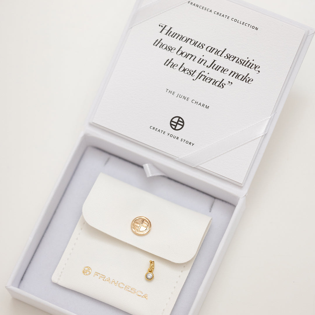 Round gold charm with bezel-set mother of pearl representing the June birthstone in white box.