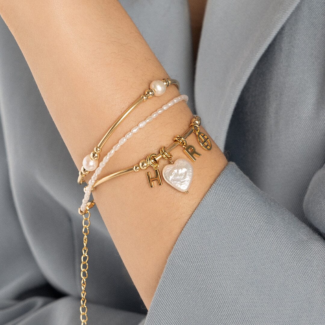 A gold charm in the shape of the letter A, attached to a bracelet, on models wrist