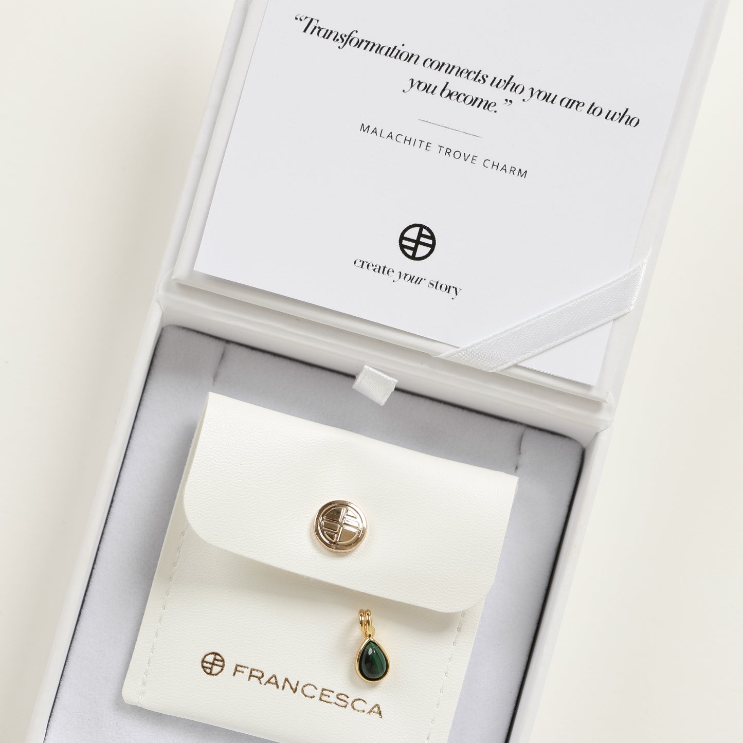 A gold charm with a teardrop-shaped malachite stone set in its centre, in a white box