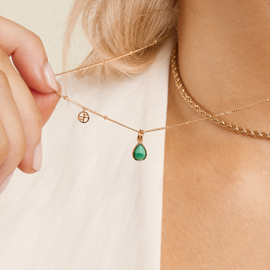 A gold charm with a teardrop-shaped malachite stone set in its centre, on a chain around the neck.